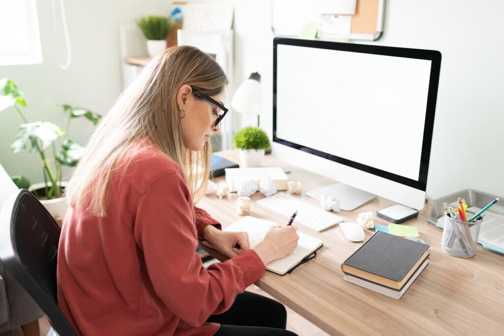 Caucasian woman working in her office and trying to write while suffering from writer's block with some crumpled papers in her desk