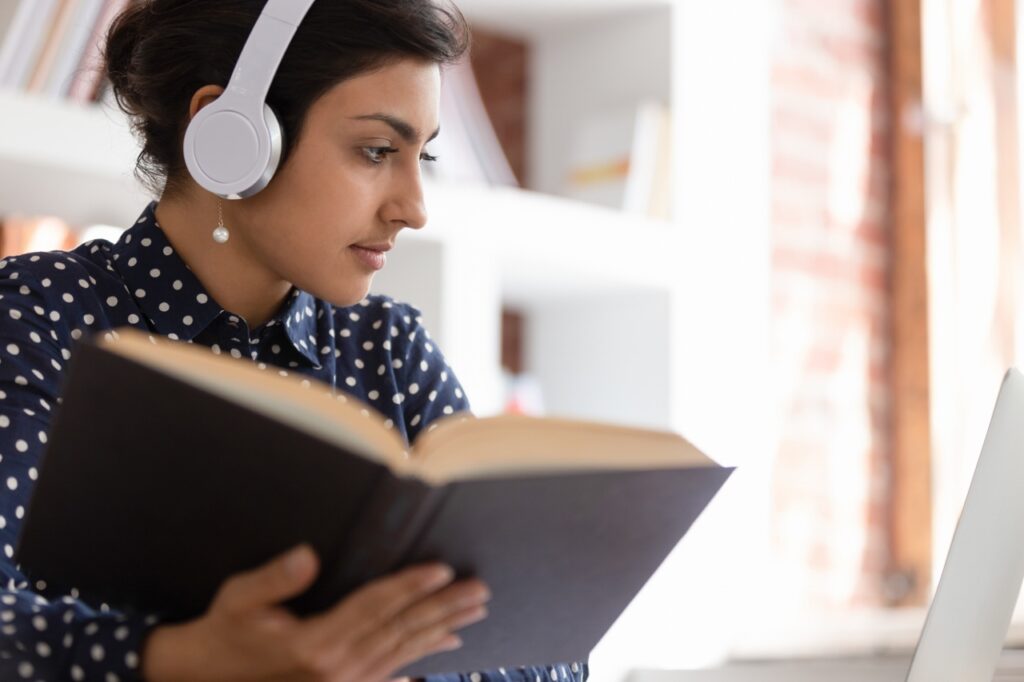 Woman holding a book is working with her laptop