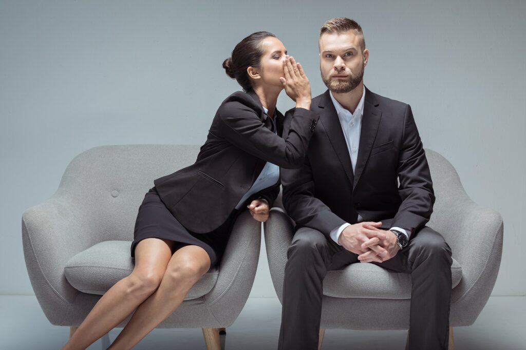 businesswoman whispering something on colleague's ear while sitting on chairs