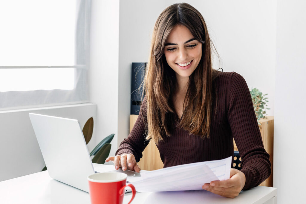 Bildungsgutschein courses Young smiling pretty adult woman working on laptop while checking home invoices or financial documents