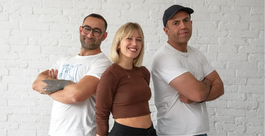 Three team members pose together on front of a white brick wall.